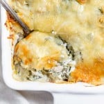 Chicken and spinach casserole in a white dish with a spoon.