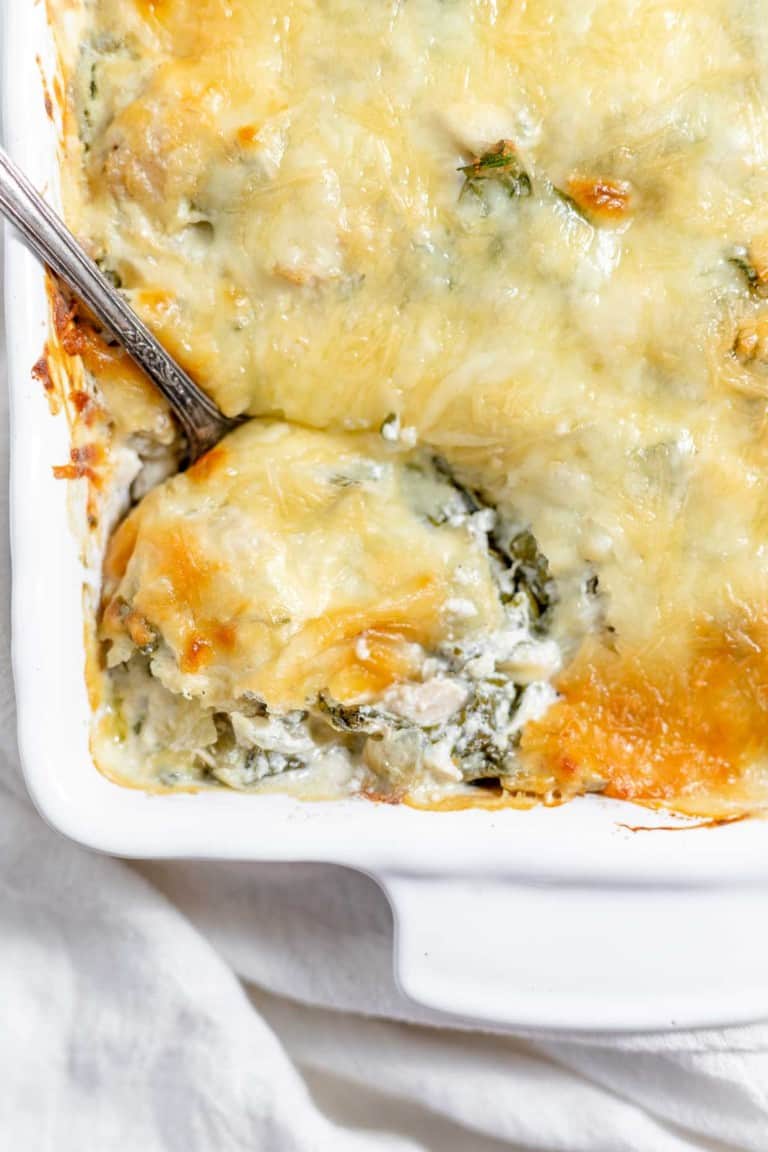 Chicken and spinach casserole in a white dish with a spoon.