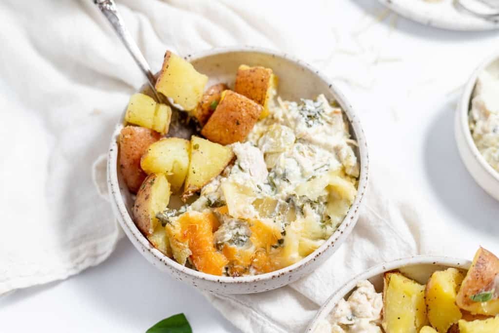 A bowl of chicken and spinach casserole with potatoes and a spoon.