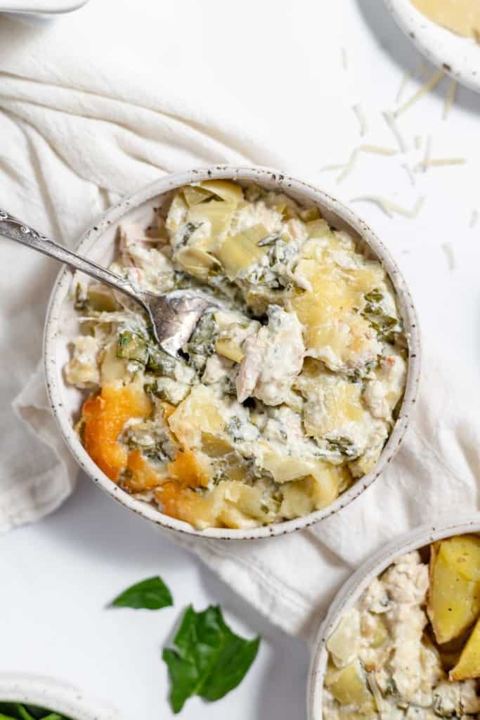 Chicken and spinach casserole in white bowls with a spoon.