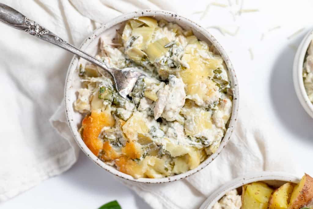 A bowl of chicken and spinach casserole with potatoes and a spoon.