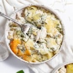 A bowl of chicken and spinach casserole with potatoes and a spoon.