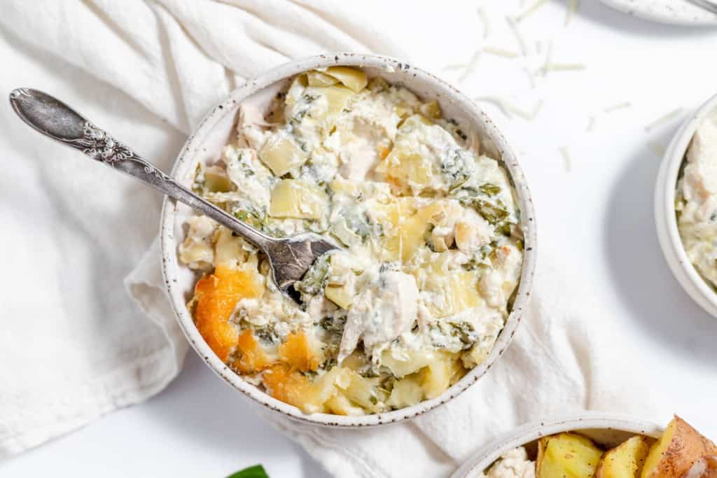Chicken and spinach casserole in a white bowl with a spoon.