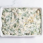 Spinach dip in a white dish on a marble countertop.