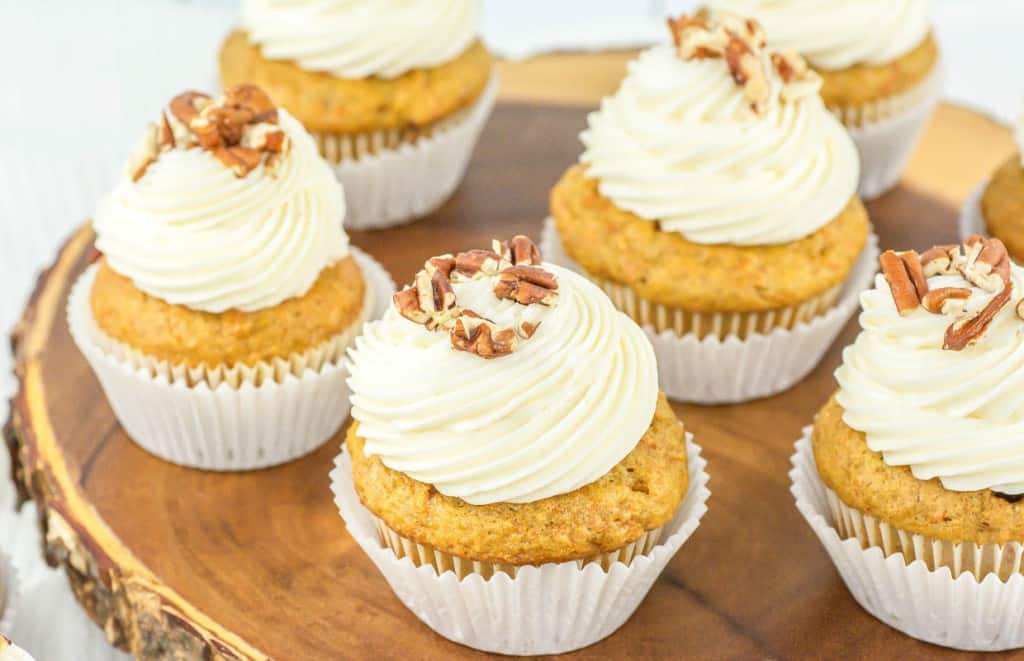 A group of frosted cupcakes topped with pecans, displayed on a wooden surface.