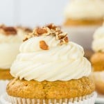 A close-up of a carrot cake cupcake topped with cream cheese frosting and chopped walnuts.