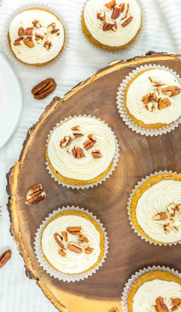 A top view of mini cheesecakes with pecan toppings arranged on a wooden slab.