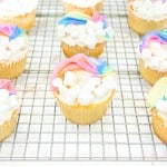 Rainbow cupcakes with marshmallows on a cooling rack.