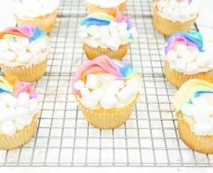 Rainbow cupcakes with marshmallows on a cooling rack.