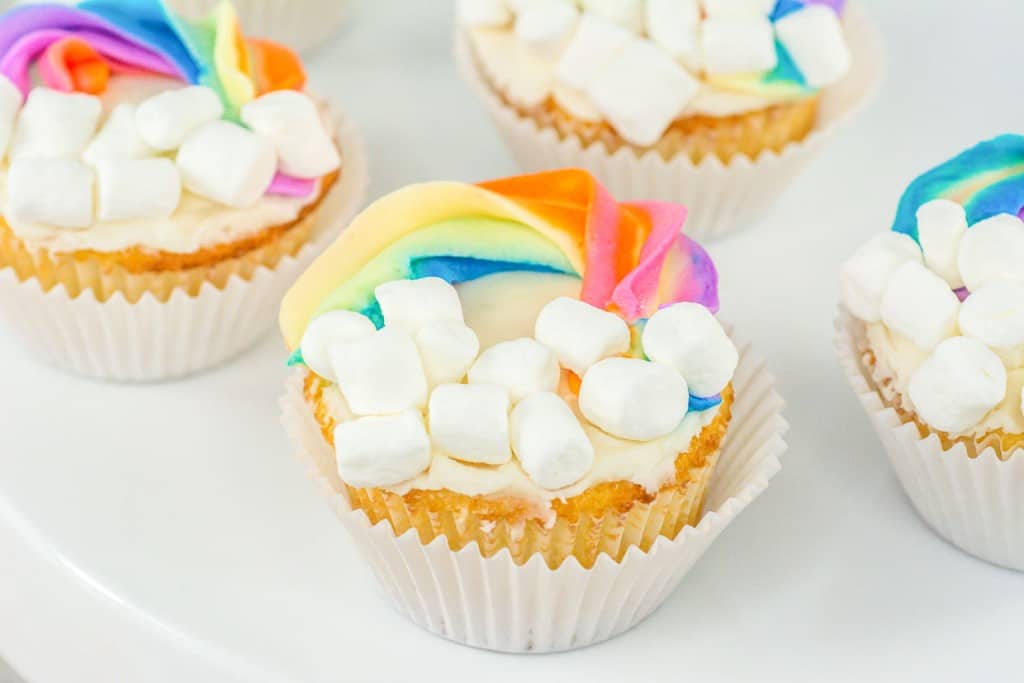 Colorful cupcakes topped with marshmallows and a rainbow-shaped decoration.