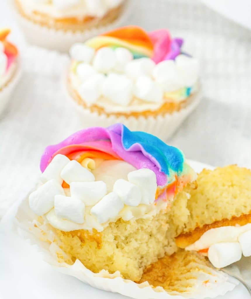 A colorful frosted cupcake with marshmallow topping partially unwrapped to reveal the inside.