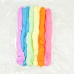 Multicolored stripes of playdough aligned side by side on a plastic surface.