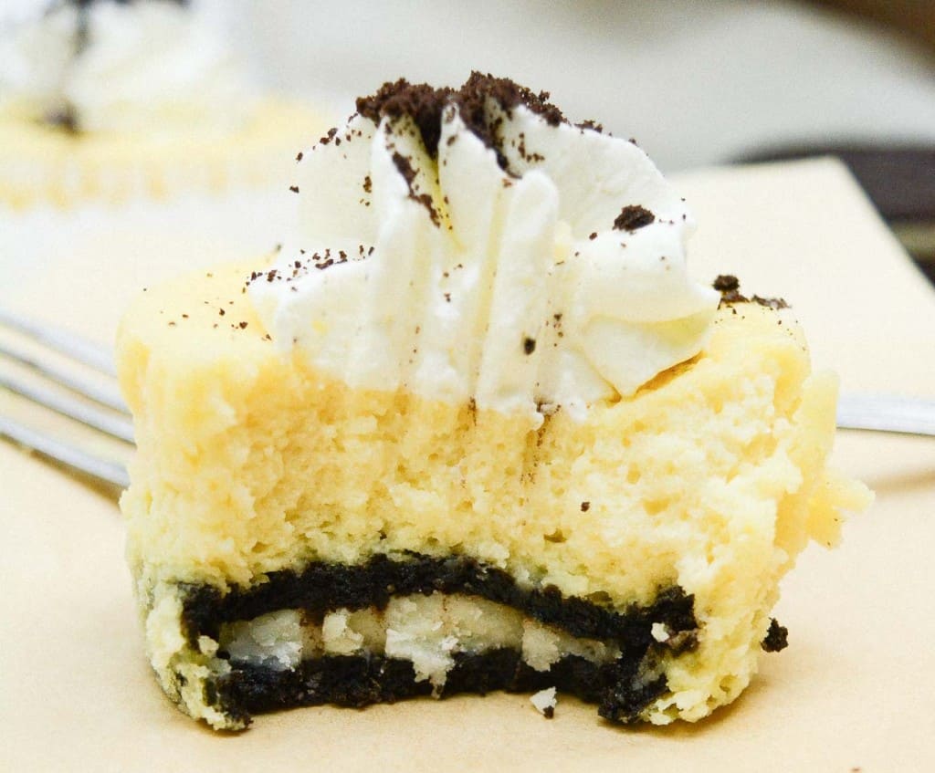 A half-eaten mini cookies and cream cheesecake on a paper sheet, with a fork.
