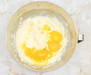 Mixing bowl with creamed butter and sugar mixture for mini cookies and cream cheesecakes with four whole eggs on top ready to be mixed in.