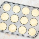 A muffin tin filled with cupcake liners and mini cookies and cream cheesecake batter, ready to be baked.