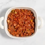 A pot of meaty tomato sauce with vegetables on a marble countertop.