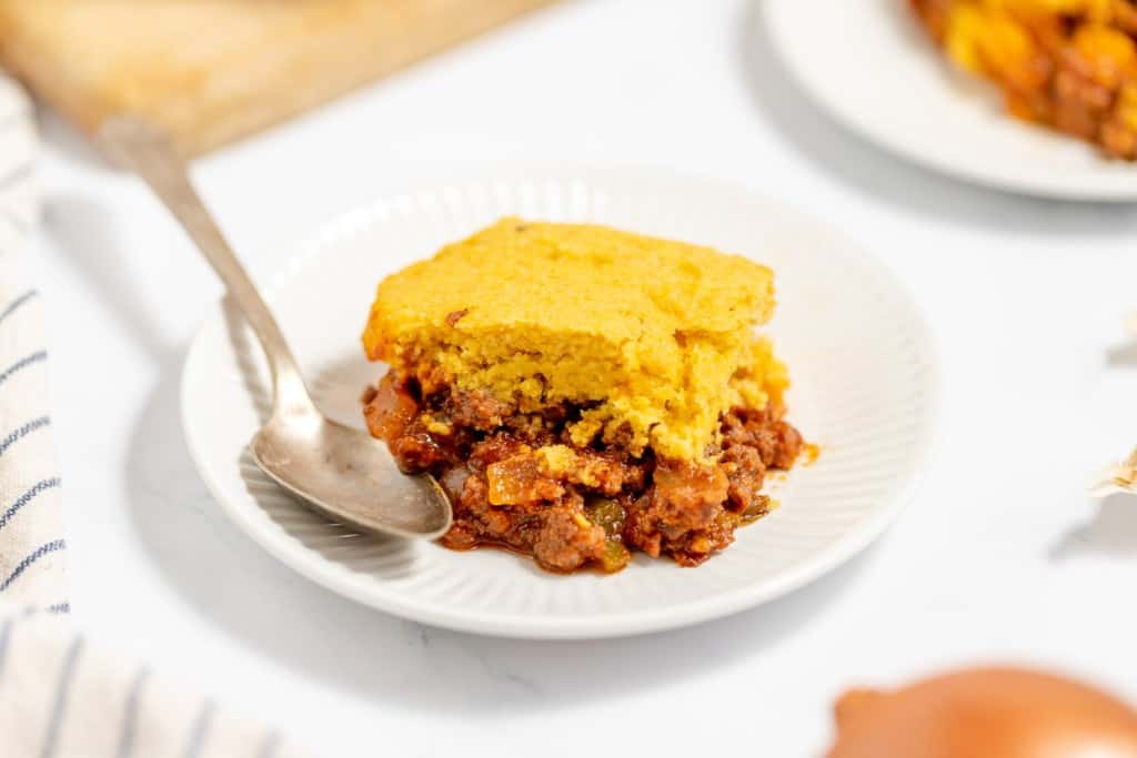 A piece of cornbread-topped casserole served on a white plate with a spoon.