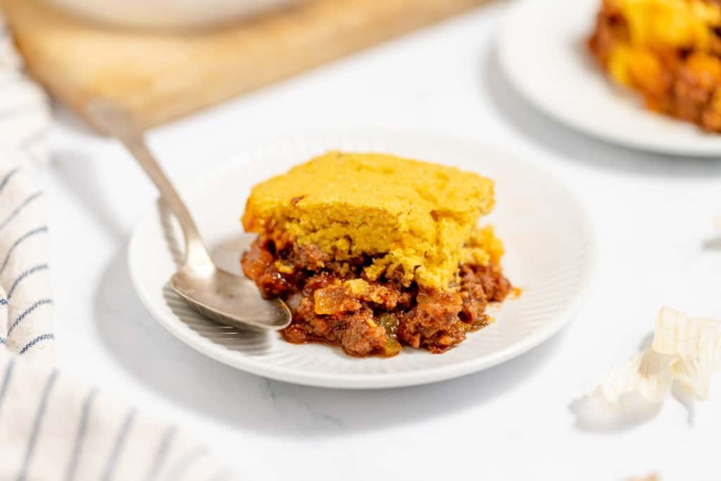 A slice of cornbread on top of chili served on a white plate with a fork.