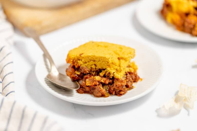 A slice of cornbread on top of chili served on a white plate with a fork.