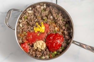 Ingredients for a dish, including ground meat, tomatoes, bell pepper, and spices, in a pot ready to be cooked.