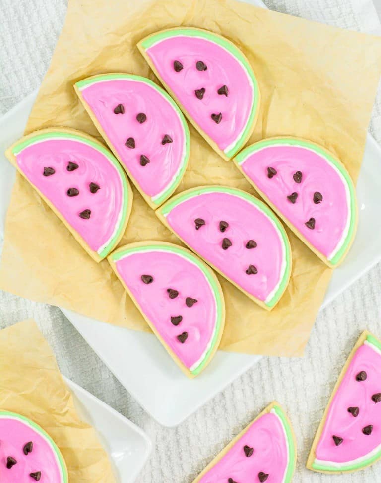 A selection of watermelon-shaped cookies with pink icing and seed details arranged on parchment paper.