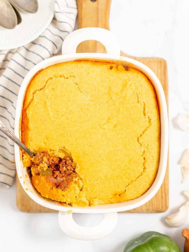A casserole dish with a golden-brown cornbread topping and a spoon scooping out the savory filling underneath.