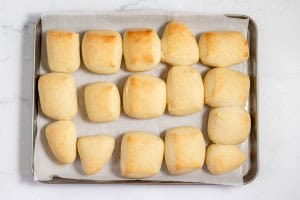 A tray of freshly baked copycat Texas Roadhouse rolls on parchment paper, arranged in rows, with a marble countertop background.