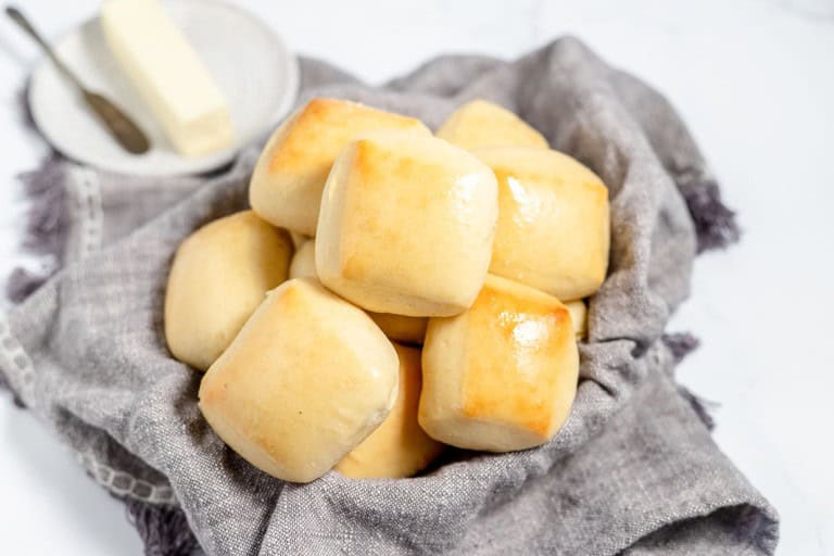Freshly baked copycat Texas Roadhouse rolls on a cloth napkin with butter in the background, displayed on a white marble surface.