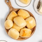 Freshly baked copycat Texas Roadhouse rolls on a wooden serving platter, accompanied by butter dishes on a marble countertop.