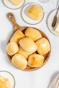 Freshly baked copycat Texas Roadhouse rolls on a wooden serving platter, accompanied by butter dishes on a marble countertop.