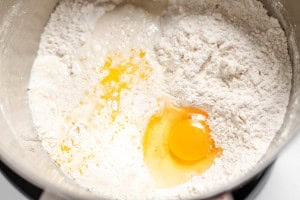 A top view of a bowl containing flour, a cracked raw egg, and liquid ingredients for baking copycat Texas Roadhouse rolls.