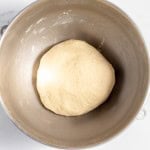 A ball of copycat Texas Roadhouse rolls dough sits in a stainless steel mixing bowl on a marble countertop.
