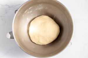 A ball of copycat Texas Roadhouse rolls dough sits in a stainless steel mixing bowl on a marble countertop.