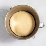 A ball of copycat Texas Roadhouse rolls dough rises in a metal mixing bowl on a marble countertop.