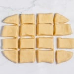Squares and triangles of unbaked copycat Texas Roadhouse rolls dough arranged in an organized pattern on a marble surface.