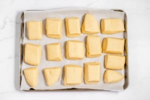 Raw square and triangular copycat Texas Roadhouse rolls arranged on a baking sheet lined with parchment paper, ready to be baked.