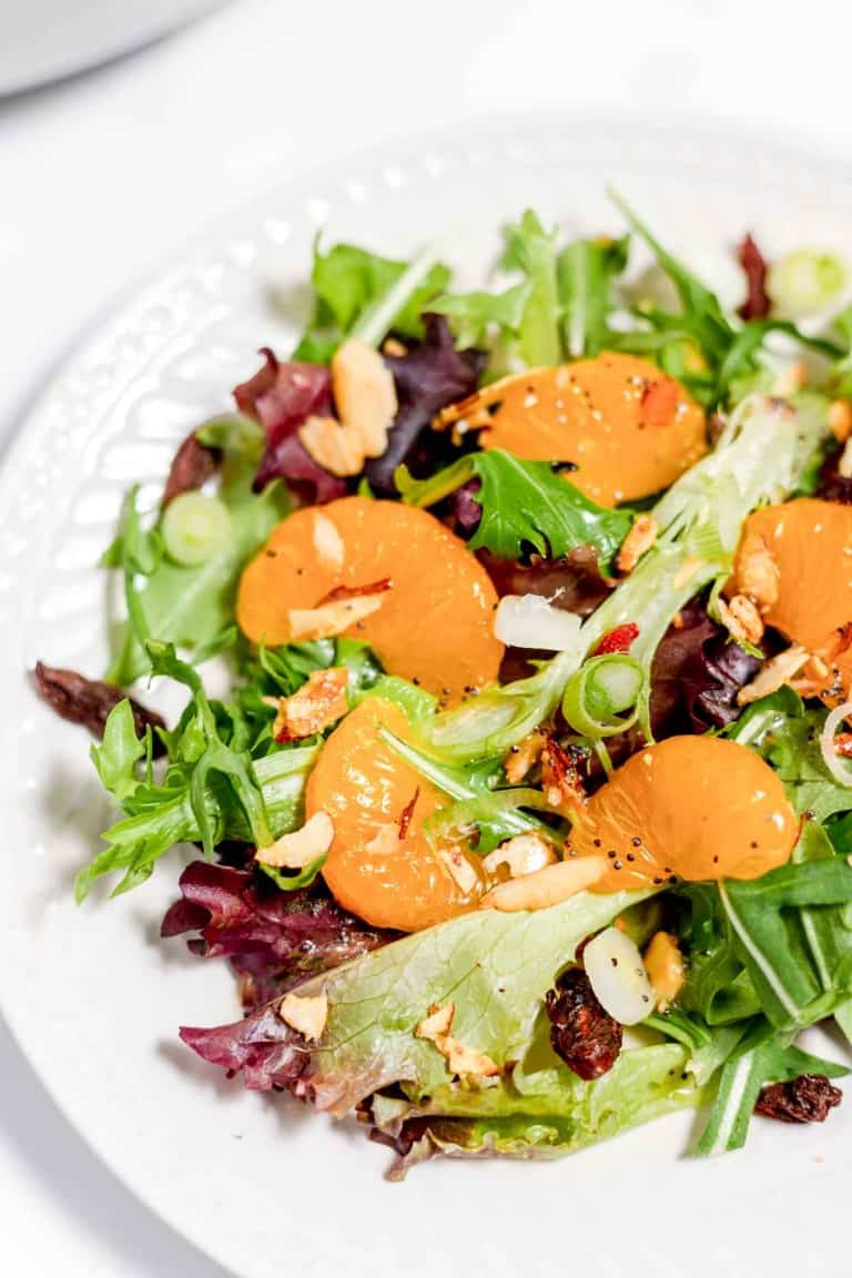 A fresh mixed greens salad with sliced apricots, nuts, and garnished with green onions on a white plate.