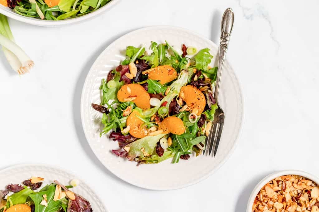 Mixed leaf salad with sliced apricots and chopped nuts on a plate.