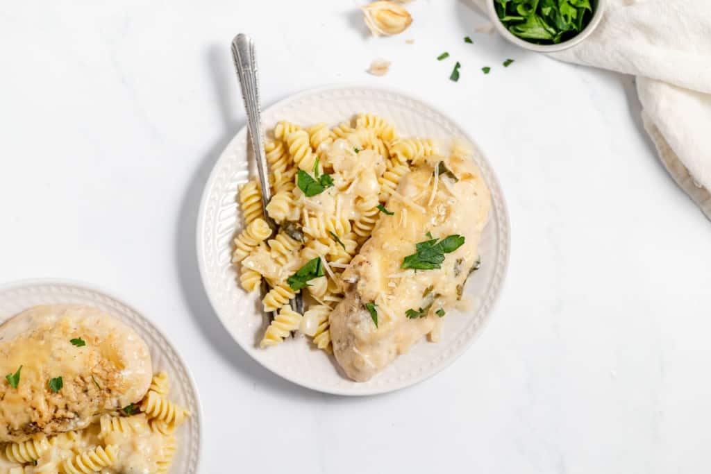 A plate of chicken breast served with fusilli pasta garnished with parsley and shredded cheese.