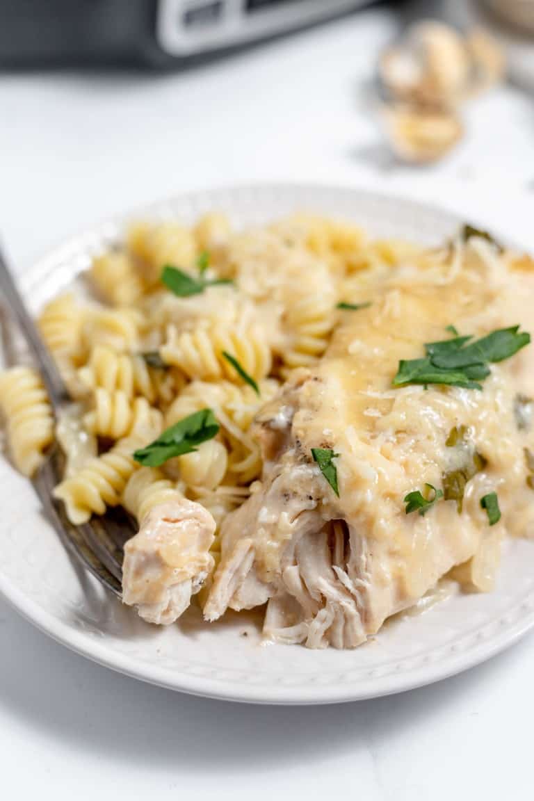 A plate of creamy chicken alfredo pasta topped with melted cheese and garnished with fresh herbs.