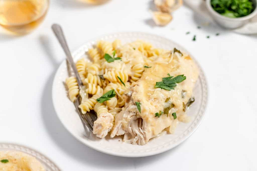 A plate of chicken alfredo pasta garnished with herbs, accompanied by a fork.