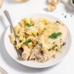 A plate of chicken alfredo pasta garnished with herbs, accompanied by a fork.