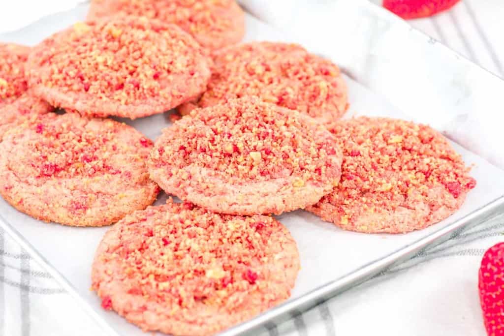 A tray of freshly baked strawberry crunch cookies on a kitchen cloth.