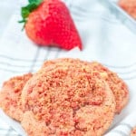 Strawberry Crunch Cookies on a striped cloth with a fresh strawberry in the background.