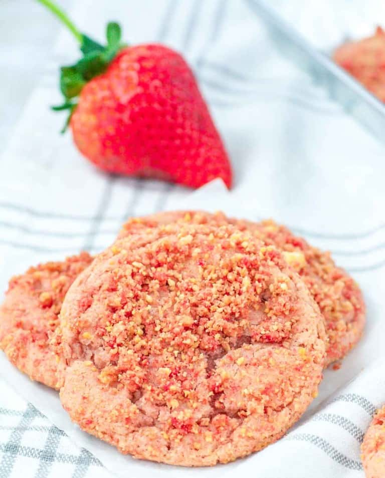 Strawberry Crunch Cookies on a striped cloth with a fresh strawberry in the background.