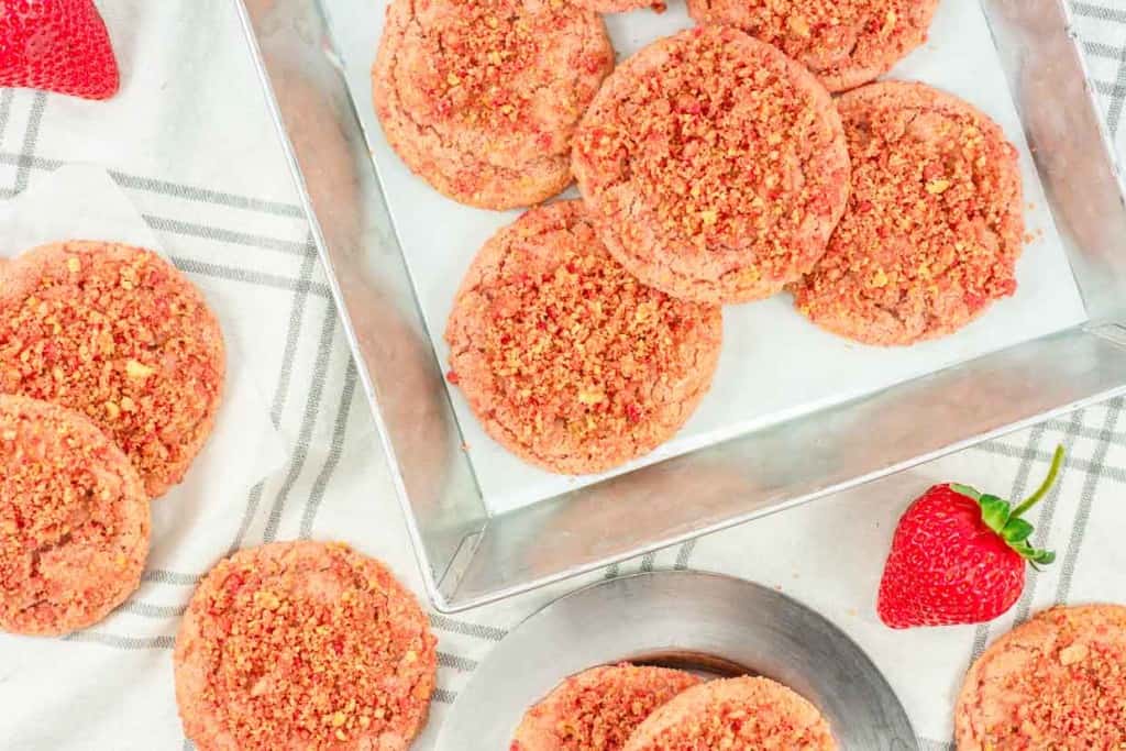 Strawberry Crunch Cookies on a baking tray with a fresh strawberry nearby.