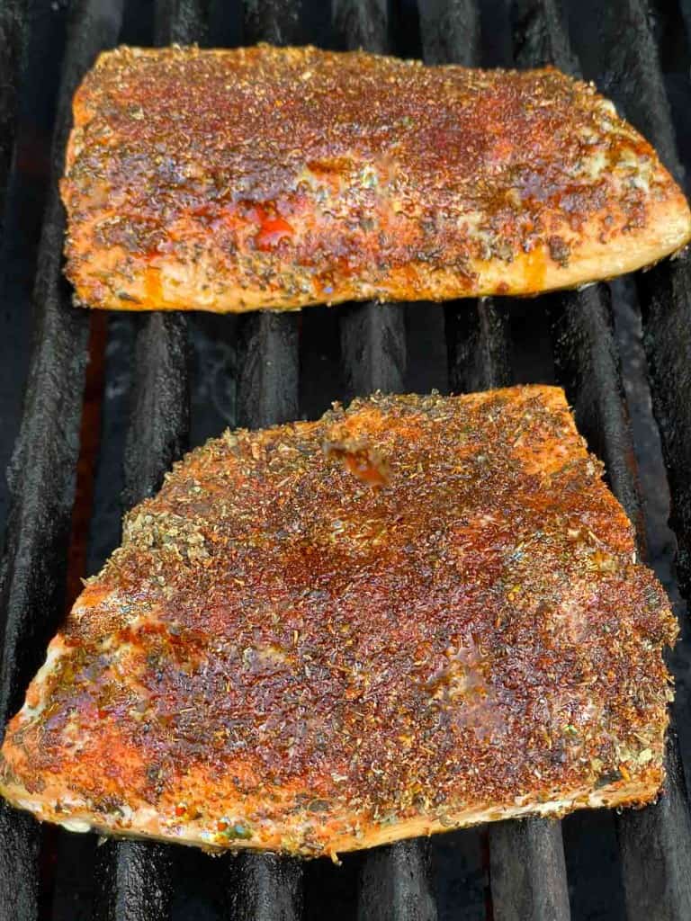 Two salmon fillets with a spice rub cooking on a barbecue grill.