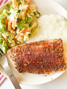 A plate with Cajun-seasoned salmon, white rice, and stir-fried vegetables.