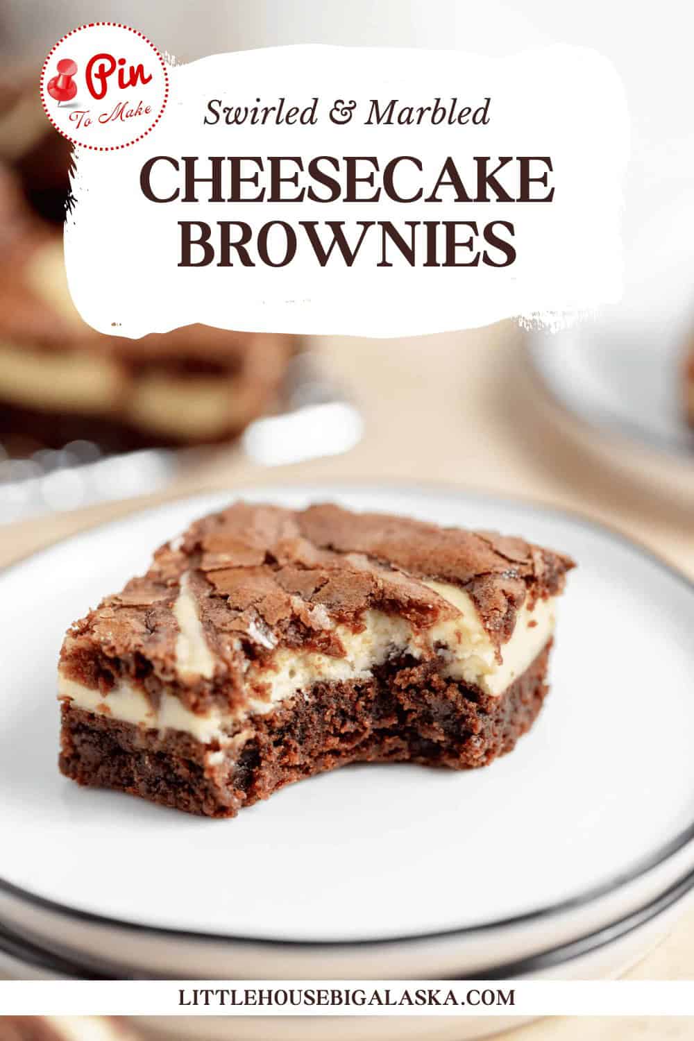 A cheesecake brownie with a bite taken out is displayed on a white plate. The text at the top reads "Swirled & Marbled Cheesecake Brownies," and the bottom credits "littlehousebigalaska.com.