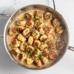 A skillet filled with cooked meatballs in a creamy sauce, garnished with chopped parsley.